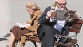 Dva penzionera sede na klupi i citaju novine